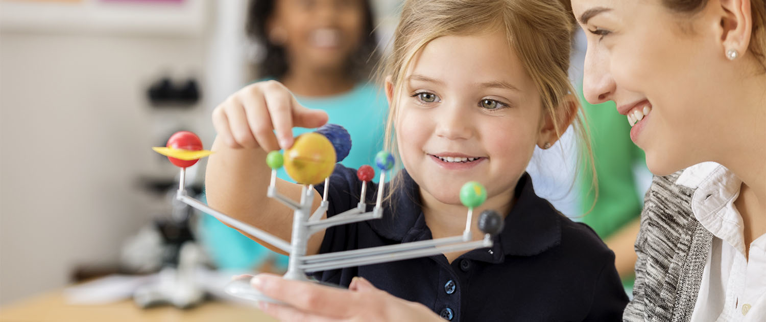 A private school student and teacher examine a solar system model